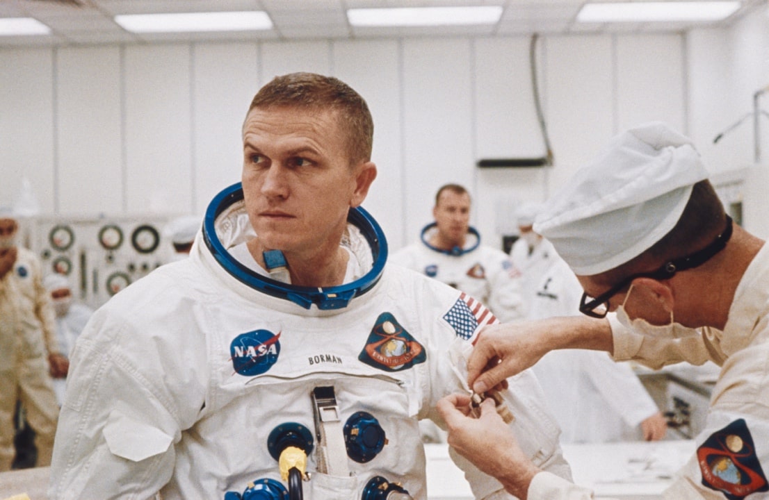 Jim Lovell looks on as a technician helps Frank get suited up